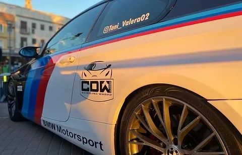 Un coche de competición BMW está aparcado delante de un edificio.
