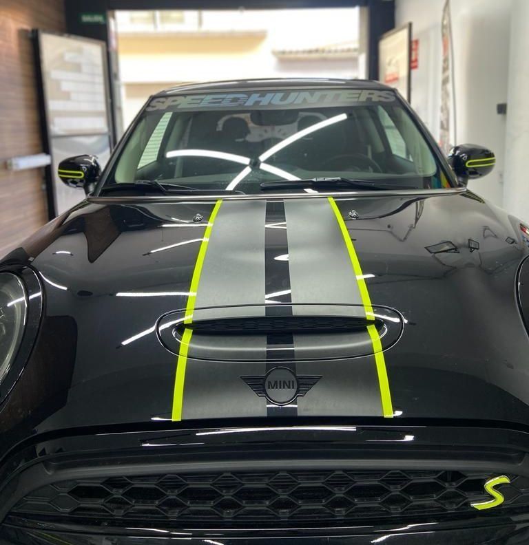 Un mini cooper negro con rayas amarillas en el capó