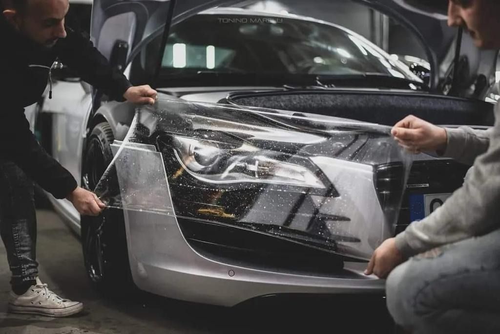 Dos hombres están envolviendo un automóvil con film plástico.