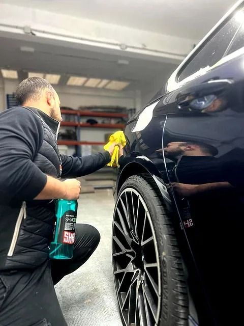 Un hombre está limpiando un coche con un paño y una botella de spray.