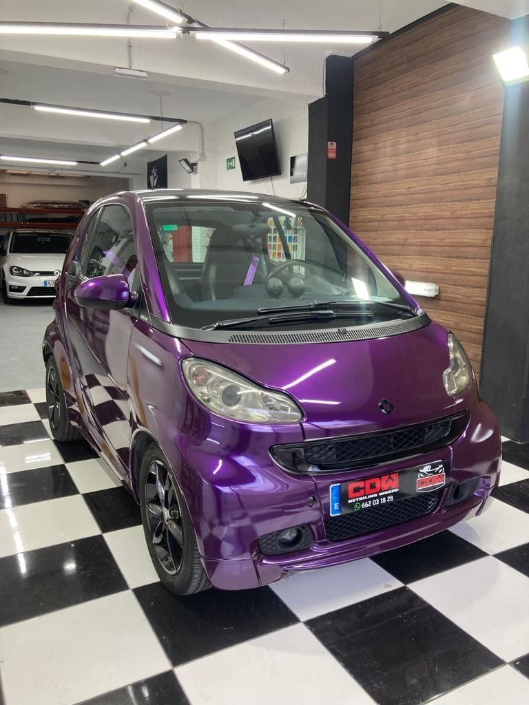Un coche morado está aparcado en un garaje sobre un suelo cuadriculado.