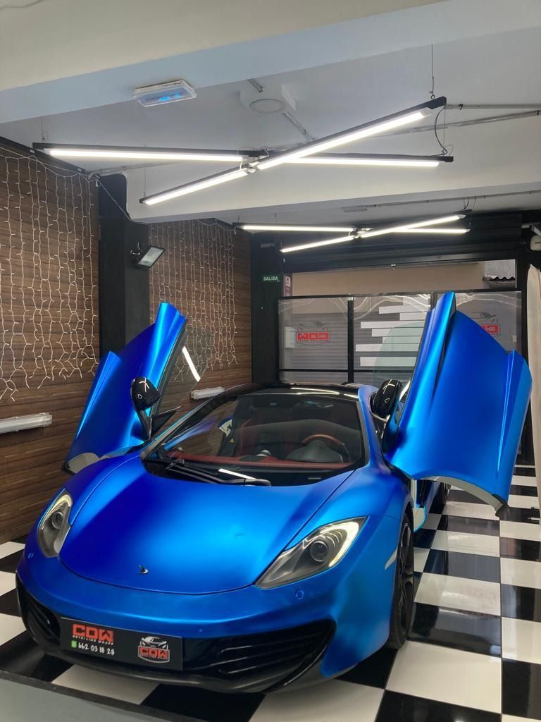 Un coche deportivo azul está aparcado en un garaje con las puertas abiertas.