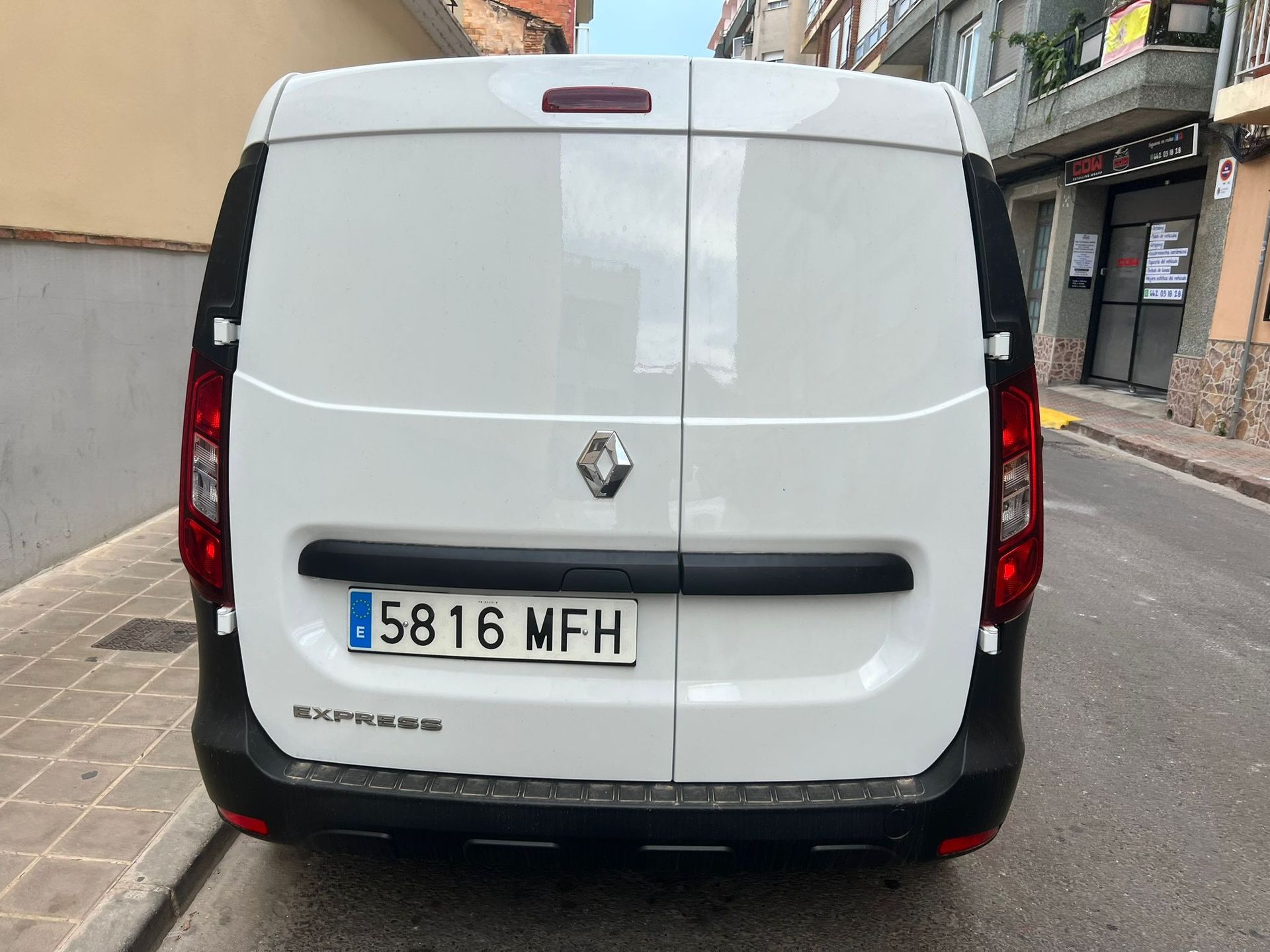 Una camioneta blanca con matrícula que dice 5816 mfh está estacionada al costado de la carretera.