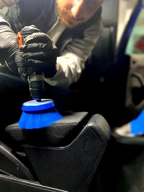 Un hombre está limpiando la consola de un automóvil con un cepillo y un taladro.