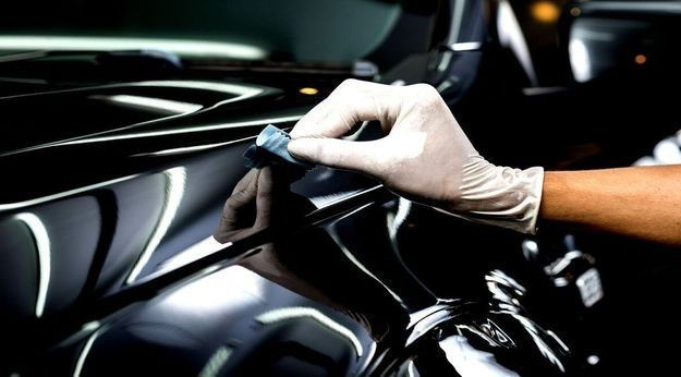 Una persona que lleva guantes está puliendo un coche negro.