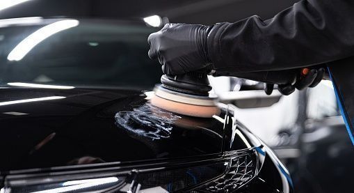 Un hombre está puliendo un coche negro con una máquina.
