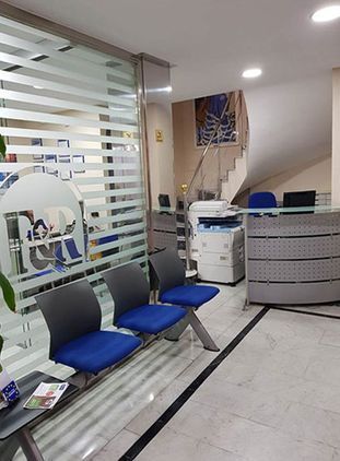 Una sala de espera con sillas azules y una pared de cristal.