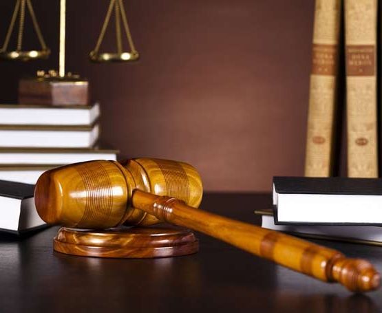 Un mazo de juez de madera está sobre una mesa al lado de libros y balanzas de la justicia.