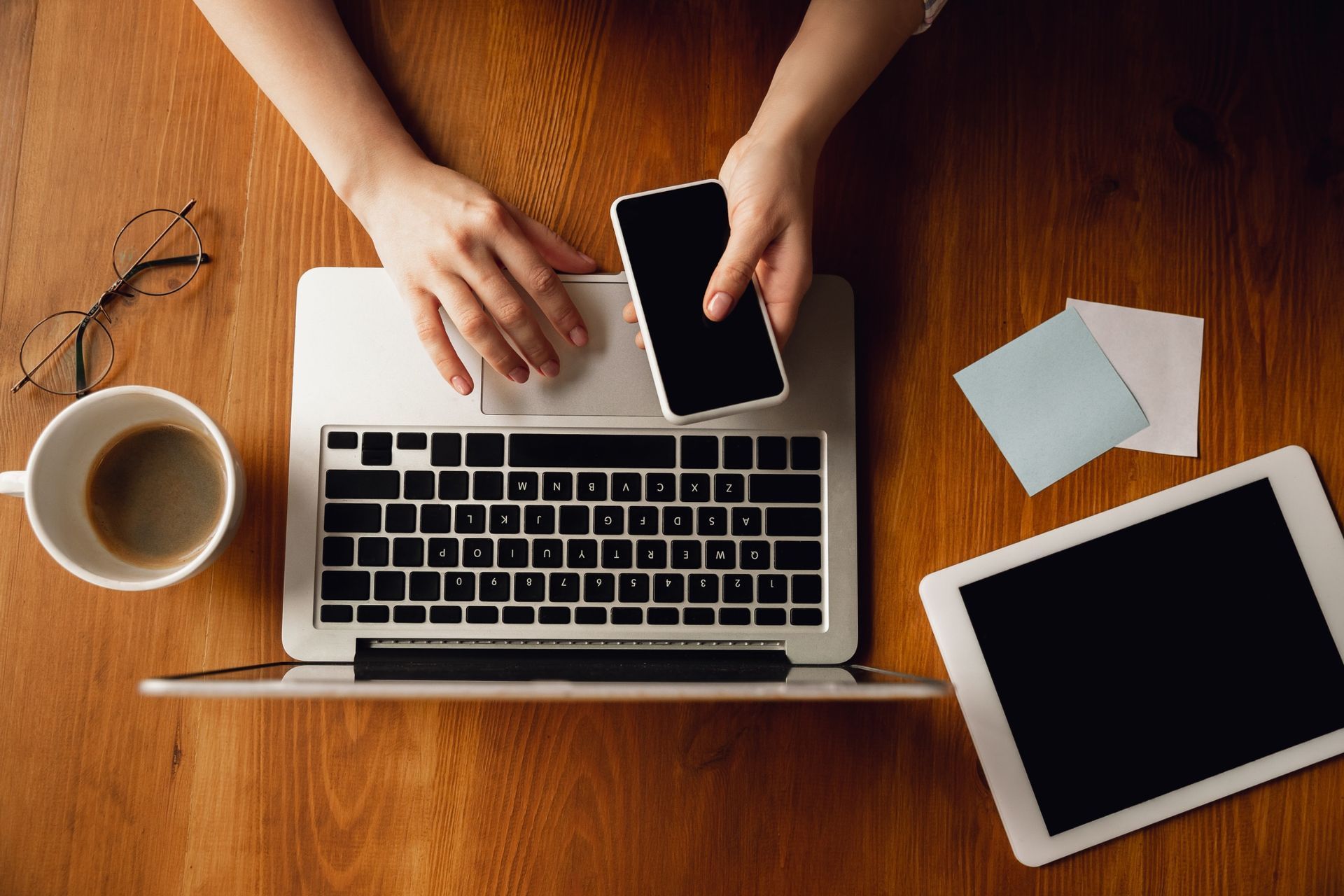 Una persona está sentada en una mesa usando una computadora portátil y un teléfono celular.
