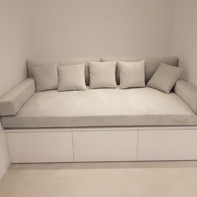 Un sofá blanco con almohadas y cajones debajo en una habitación.