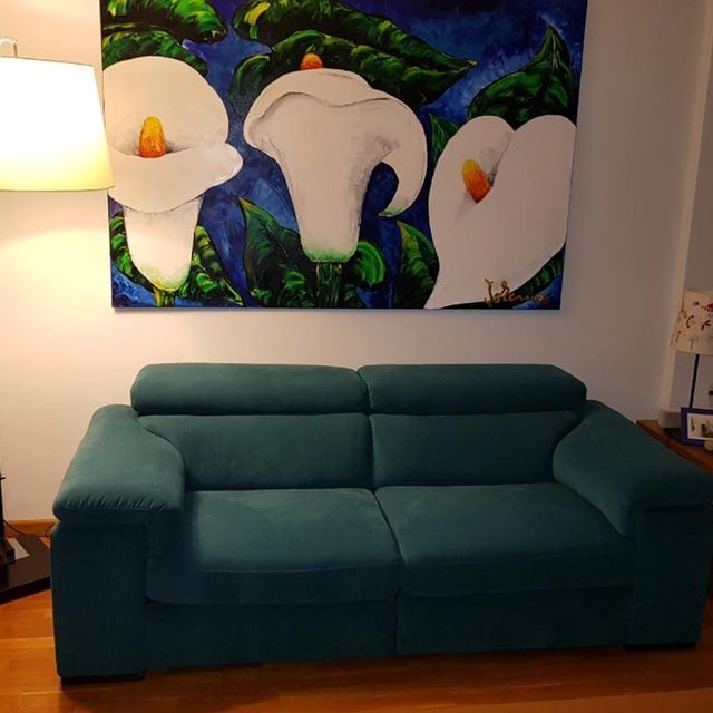 Un cuadro de flores blancas cuelga sobre un sofá verde.