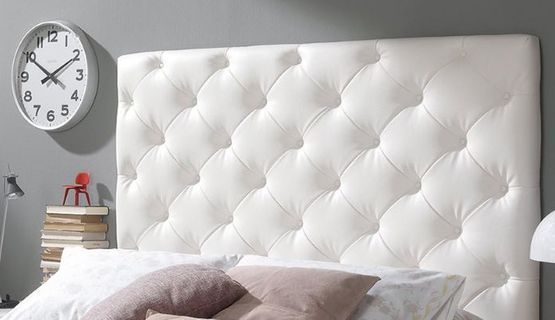 Una cama con un cabecero blanco y un reloj en la pared encima.