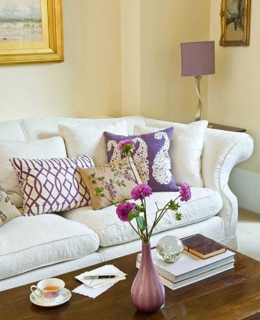 Una sala de estar con un sofá blanco y almohadas moradas.