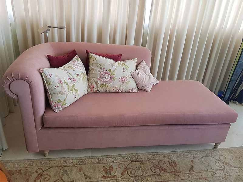 Una tumbona rosa con almohadas está situada frente a una ventana.