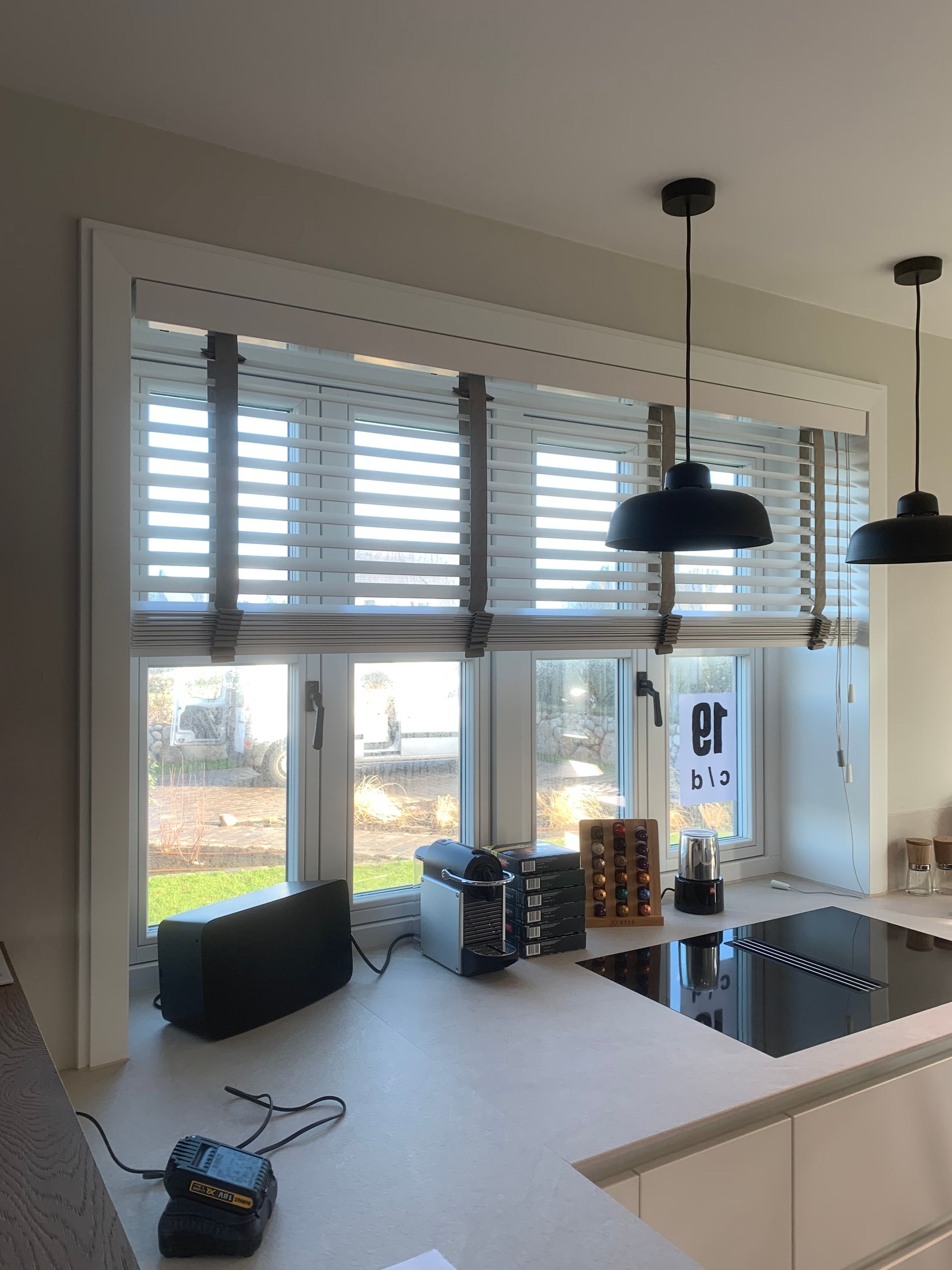 Küchenfenster mit horizontalen Jalousien, schwarzen Pendelleuchten und Küchengeräten auf der Arbeitsplatte.