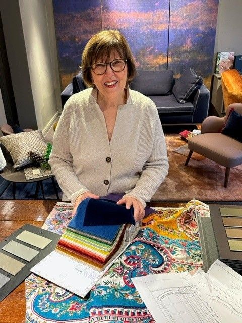Eine Person lächelt, während sie Stoffmuster an einem Tisch mit Designproben in einem Ausstellungsraum in der Hand hält.