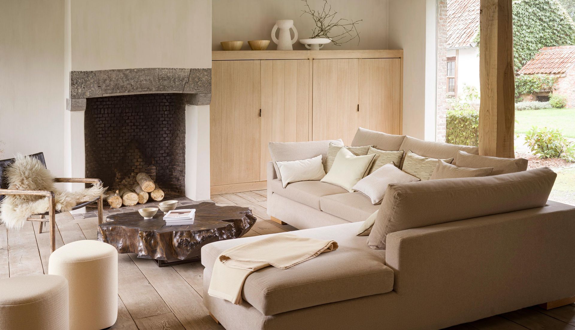 Gemütliches Wohnzimmer mit Kamin, beigefarbenem Ecksofa, Couchtisch aus Holz und neutraler Farbgestaltung.