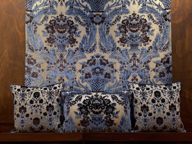 Drei Kissen mit blau-weißem Damast-Blumenmuster vor einem passenden Stoffhintergrund.