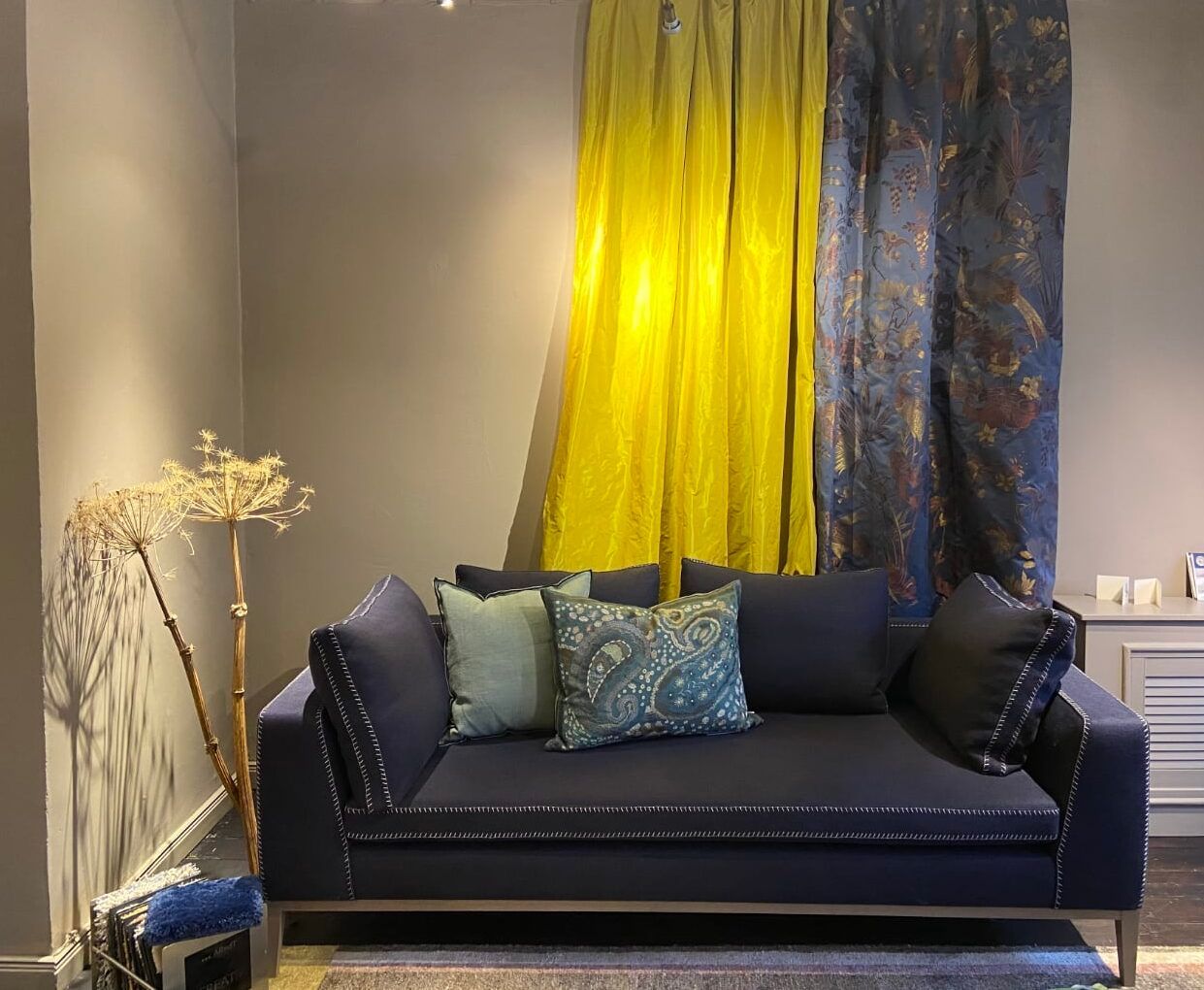 Marineblaues Sofa mit hellblauen und gemusterten Kissen, gelben und blauen Vorhängen.