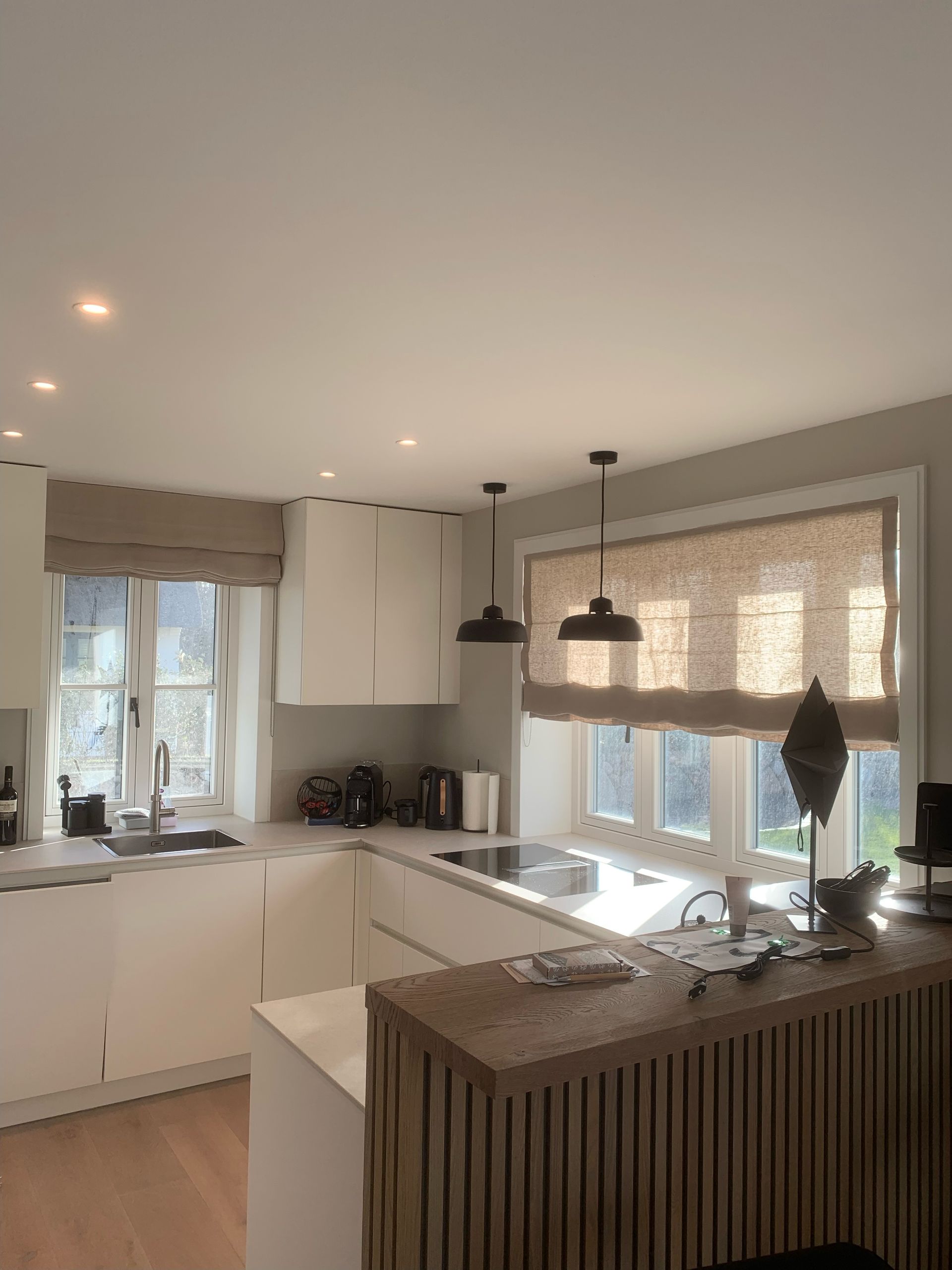 Moderne weiße Küche mit Jalousien, Pendelleuchten und Holzbar.