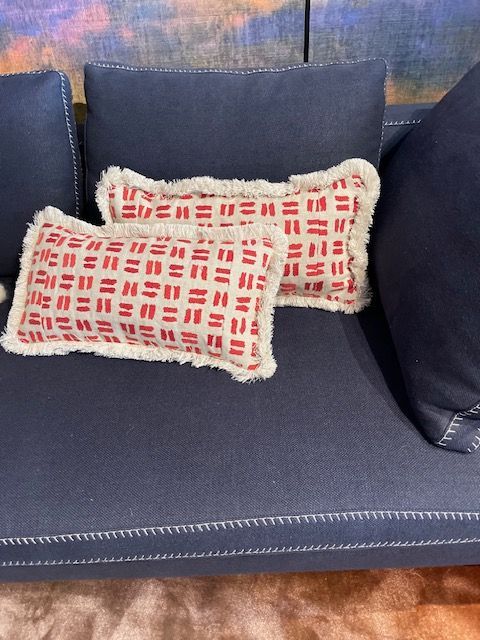 Auf einem marineblauen Sofa liegen zwei rot-weiß gemusterte rechteckige Kissen mit weißen Fransen.