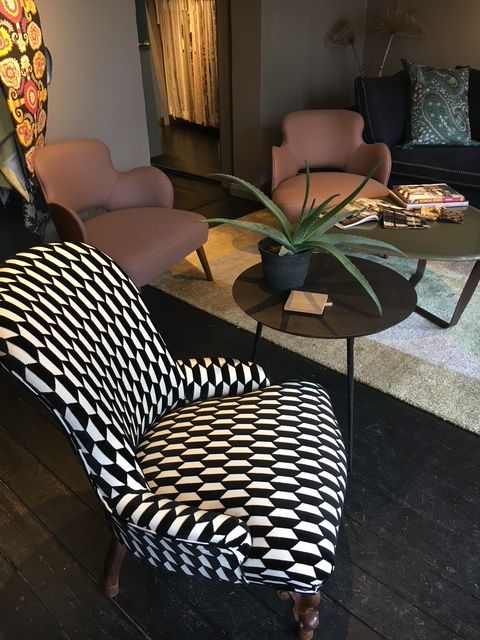 Wohnzimmer mit gemustertem Stuhl, rosa Sesseln und einem kleinen Tisch mit einer Pflanze.