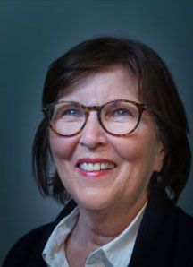 Frau mit kurzen braunen Haaren und Brille lächelt.