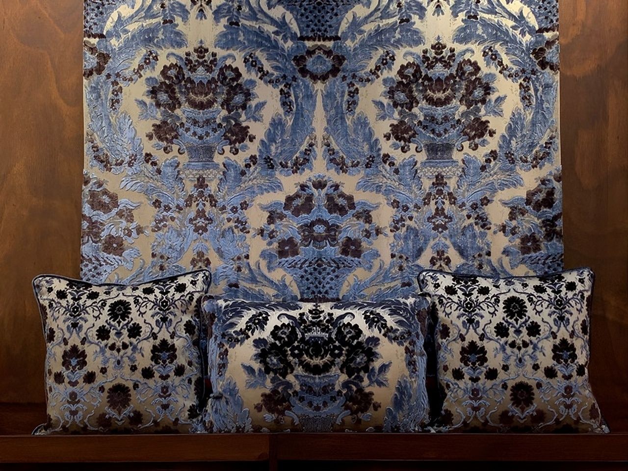 Drei gemusterte Kissen liegen vor einem großen, vertikal ausgerichteten Stoffpaneel mit einem blau-weißen Blumenmuster.