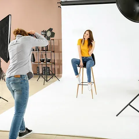 Un hombre está tomando una fotografía de una mujer sentada en un taburete en un estudio fotográfico.