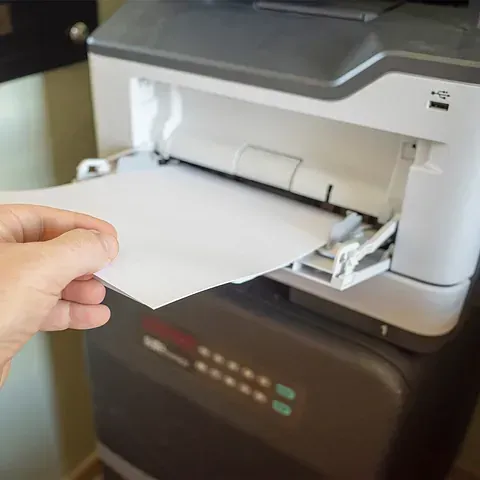 Una persona sostiene un trozo de papel delante de una impresora.