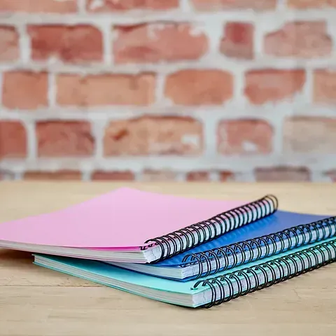Tres cuadernos en espiral están apilados uno encima del otro sobre una mesa de madera.