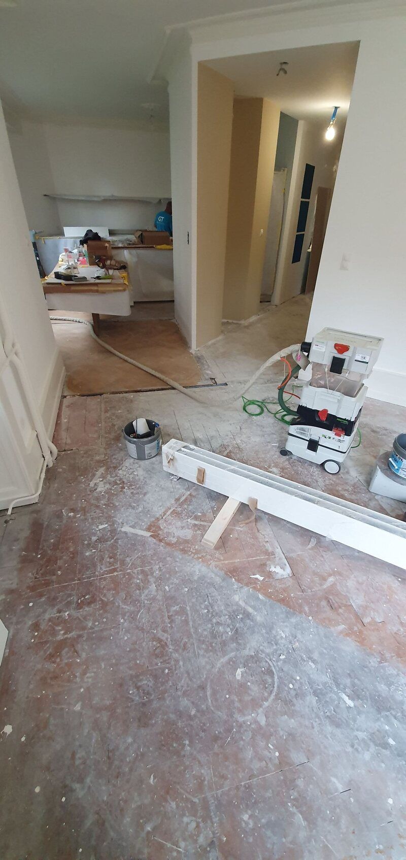 Une pièce avec un parquet au sol et un aspirateur au sol.