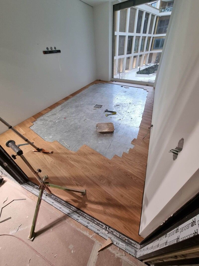 Une pièce avec du parquet en cours de pose et une fenêtre.