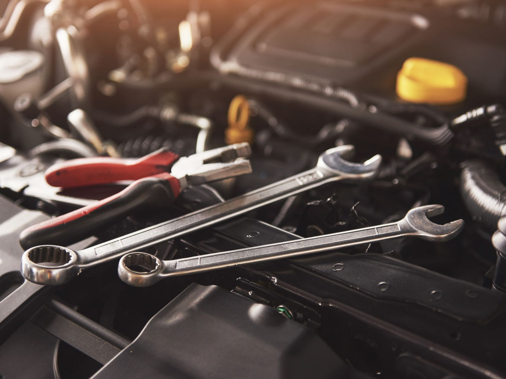 Outils de garagiste posés sur le moteur d'une voiture au capot ouvert.