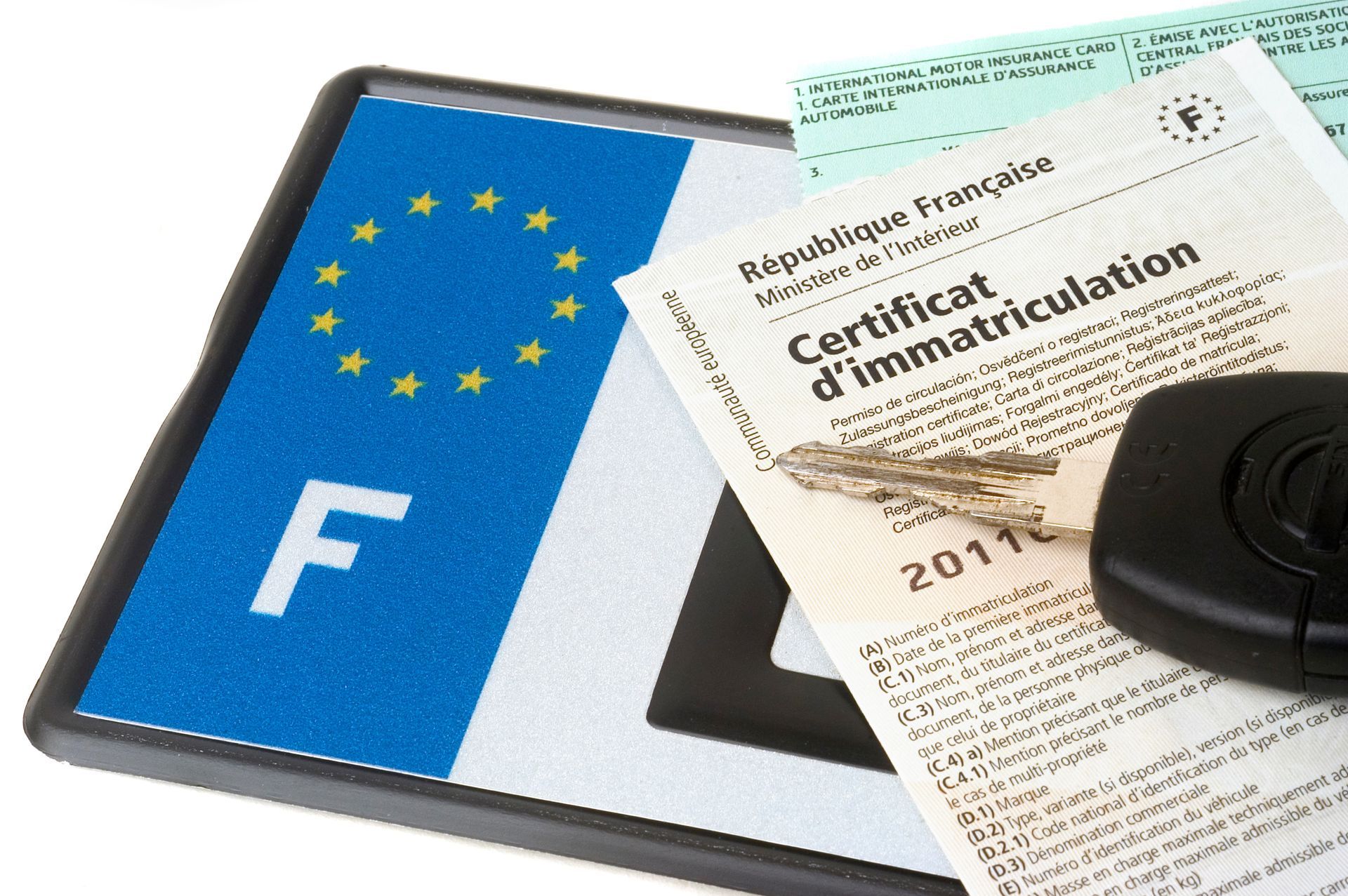 Carte grise française à côté d'une plaque d'immatriculation européenne bleue et d'une clé de voiture.
