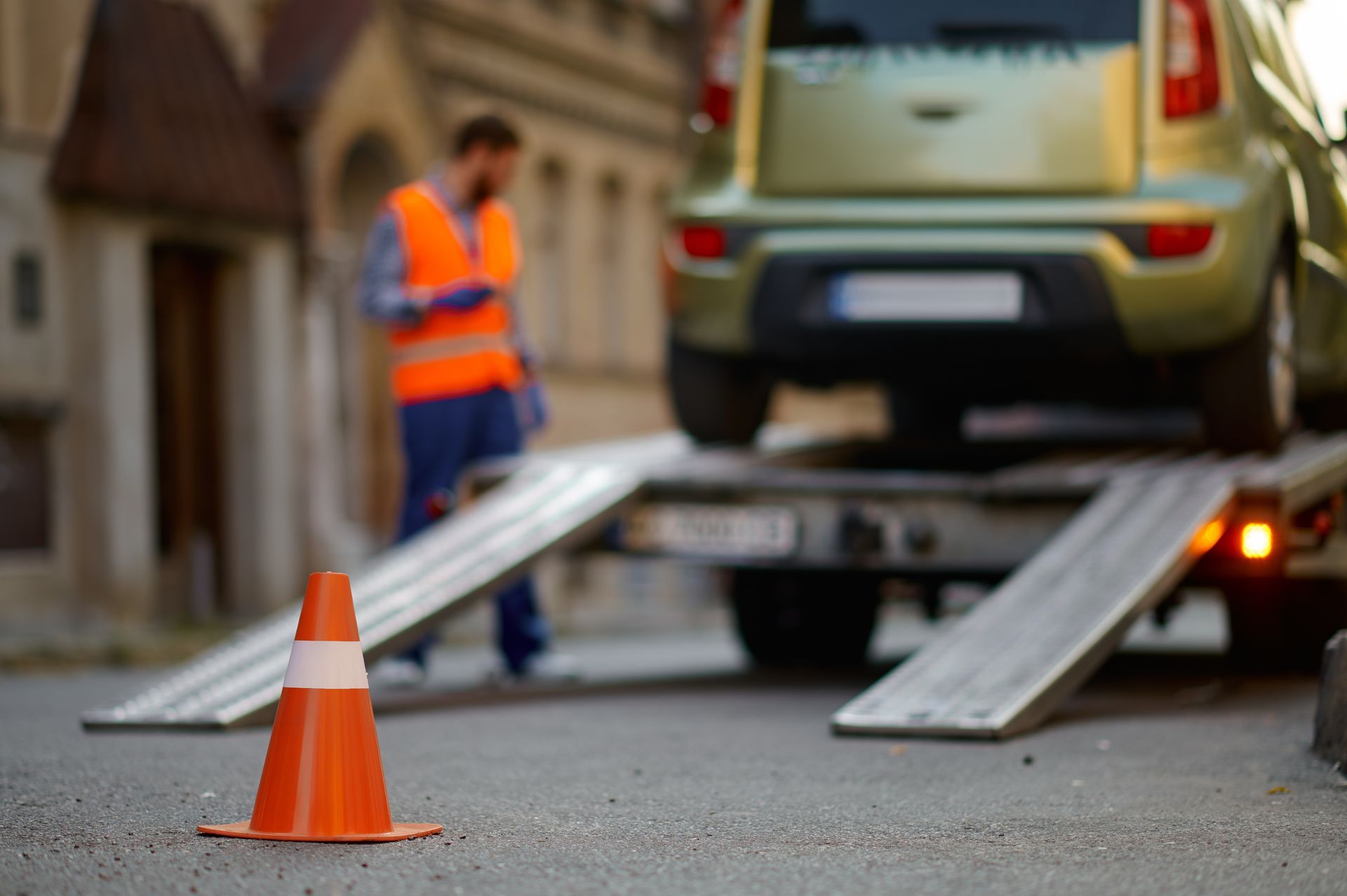 Dépanneuse chargeant une voiture avec un employé en gilet de sécurité orange, cône de signalisation au premier plan.