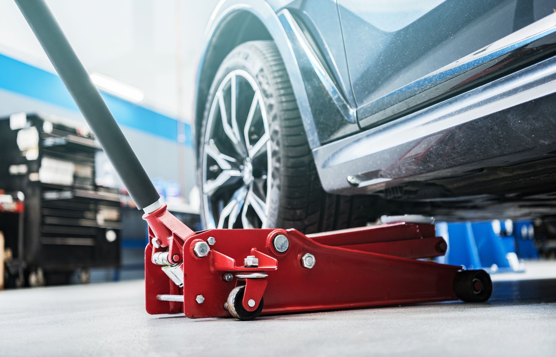 Cric rouge soulevant une voiture dans un garage, gros plan sur la roue et le châssis.