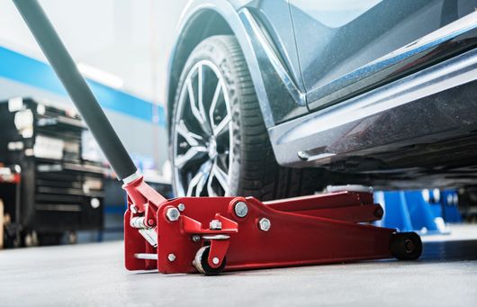 Un cric rouge soulève un véhicule noir dans un atelier de garage.