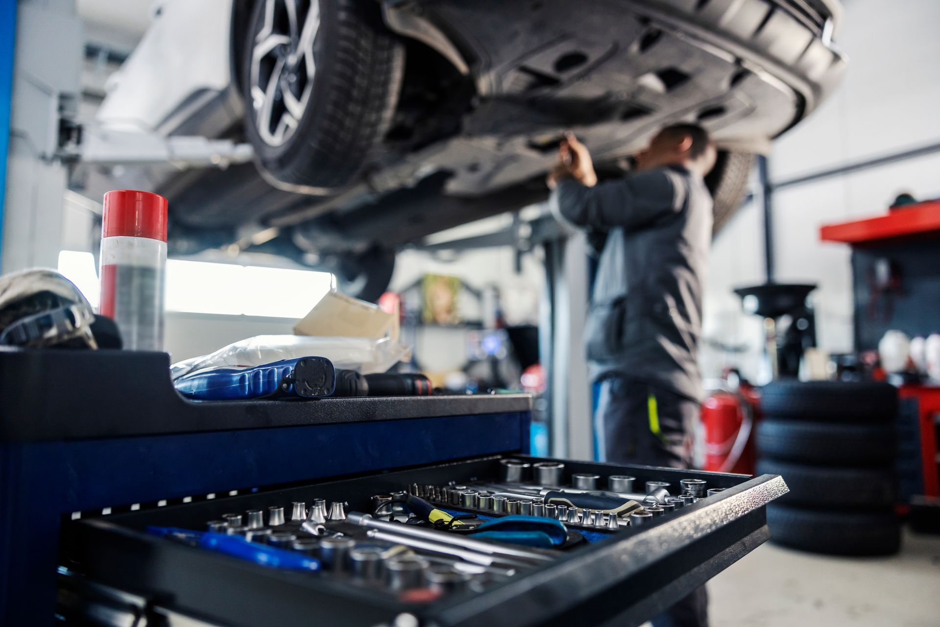 Un mécanicien travaille sous une voiture surélevée dans un atelier de réparation automobile, avec des outils au premier plan.