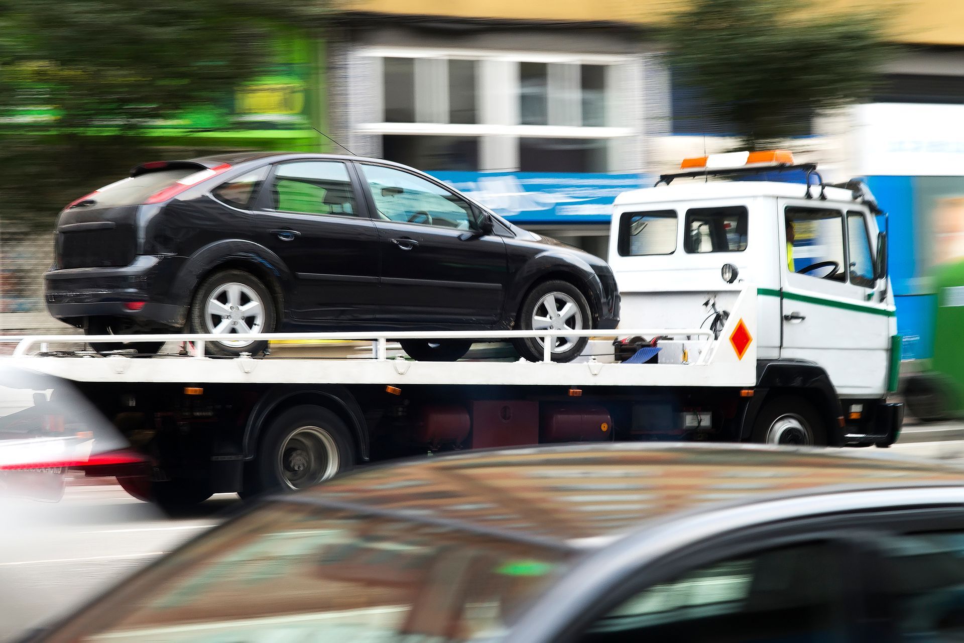 Une dépanneuse transporte une berline noire dans une rue de la ville, avec un effet de flou de mouvement.