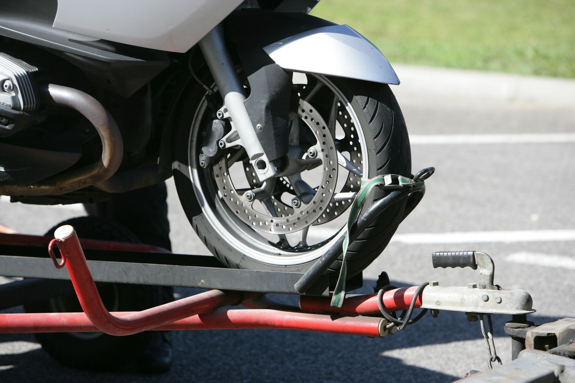 Moto attachée à un porte-moto rouge, gros plan de la roue avant sur la route.