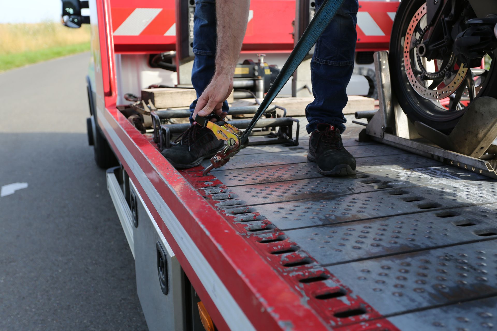 Un dépanneur arrime une moto sur un camion à plateau rouge en bordure de route.