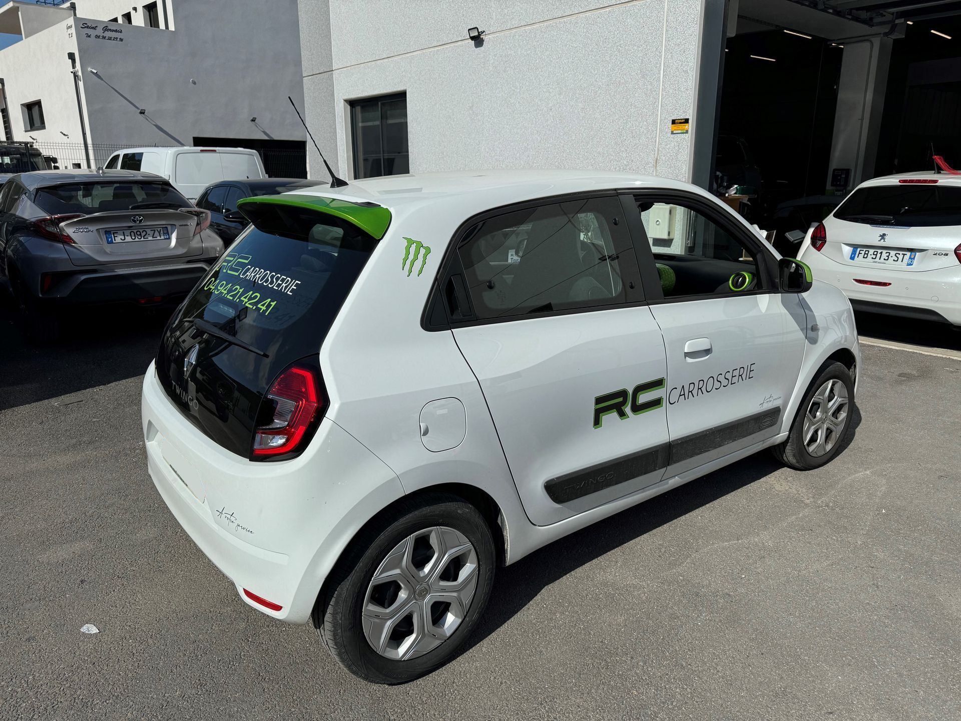 Voiture blanche avec des touches de vert et le logo de RC Rental garée à l'extérieur.