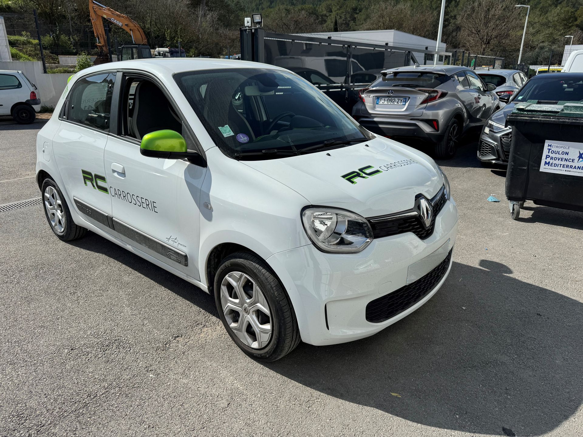 Renault Twingo électrique blanche avec des touches de vert, garée sur un parking, logo sur le côté.