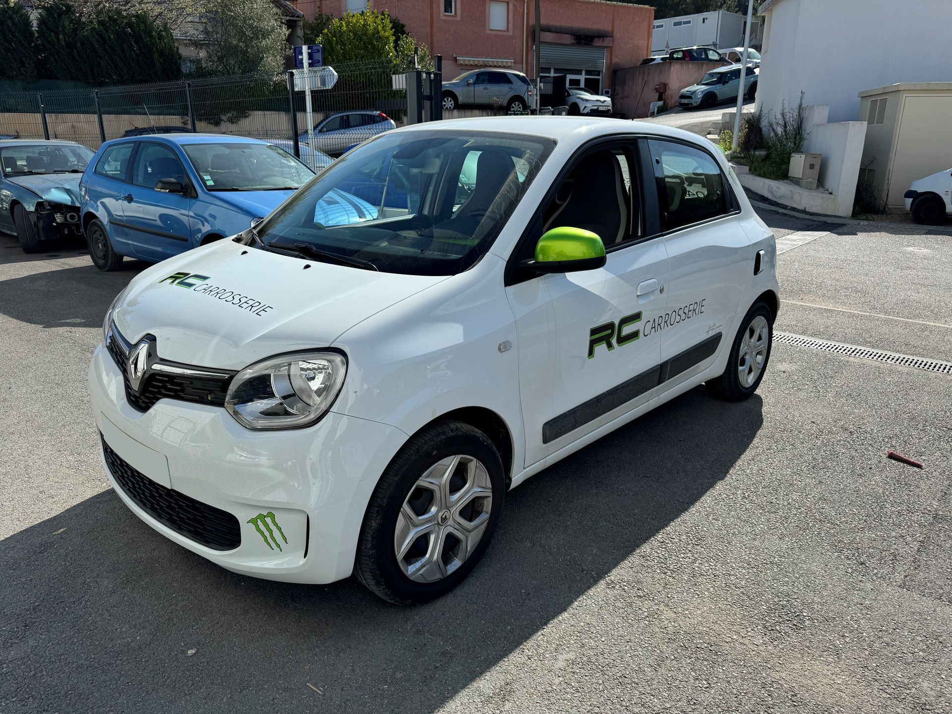 Renault Twingo blanche avec des touches de vert, garée à l'extérieur, logo sur le côté.
