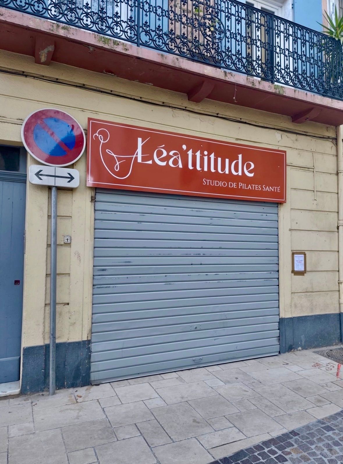 Restaurant « Lea'ttitude », volet gris fermé. Panneau marron, panneau « stationnement interdit », façade jaune.