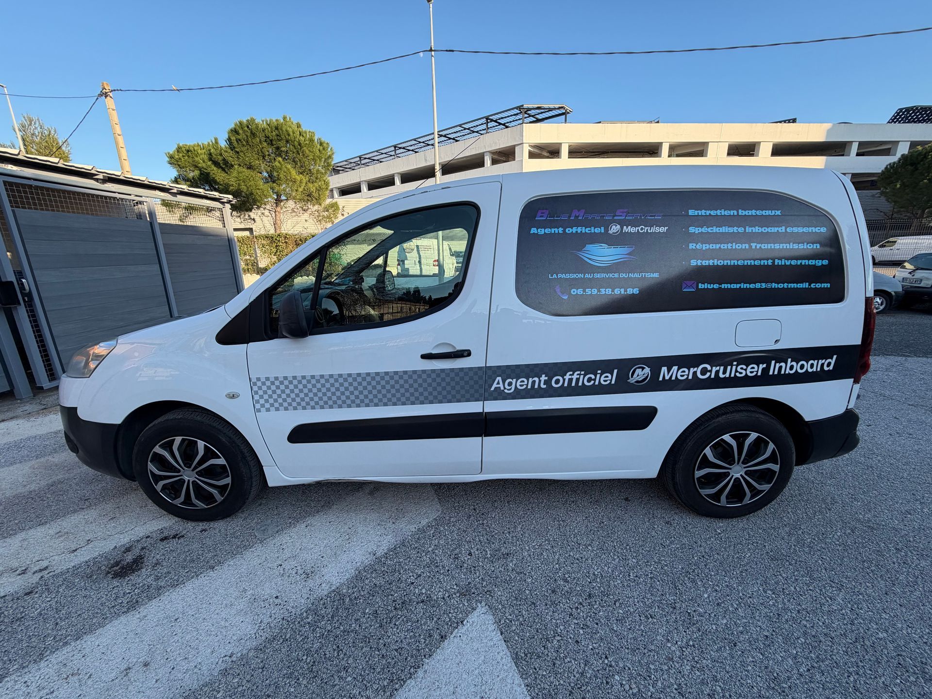 Camionnette blanche avec des graphismes noirs garée sur un passage piéton, logo d'entreprise sur le côté.