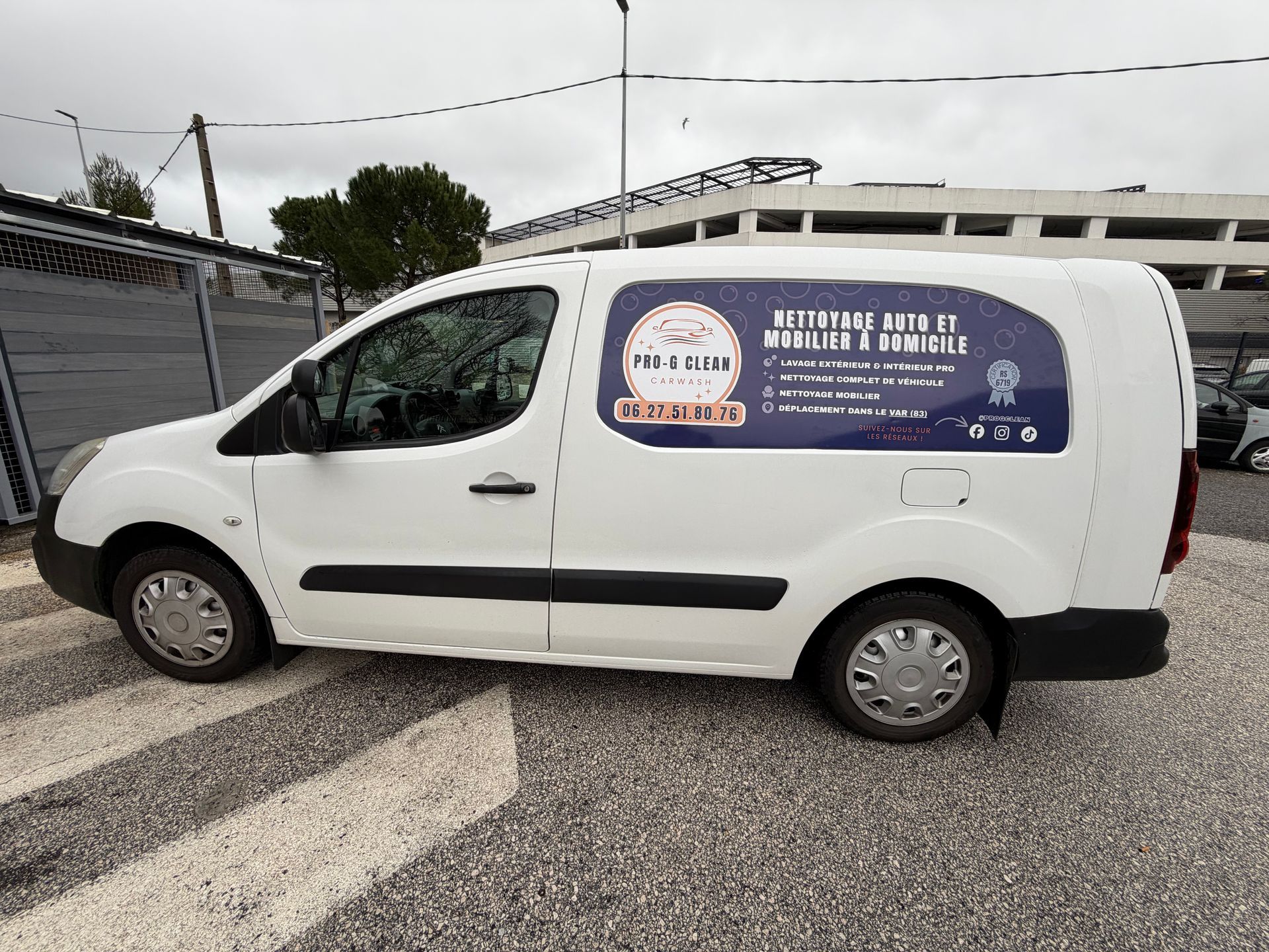 Fourgonnette blanche utilitaire avec publicité de l'entreprise, stationnée à l'extérieur sur une aire pavée.