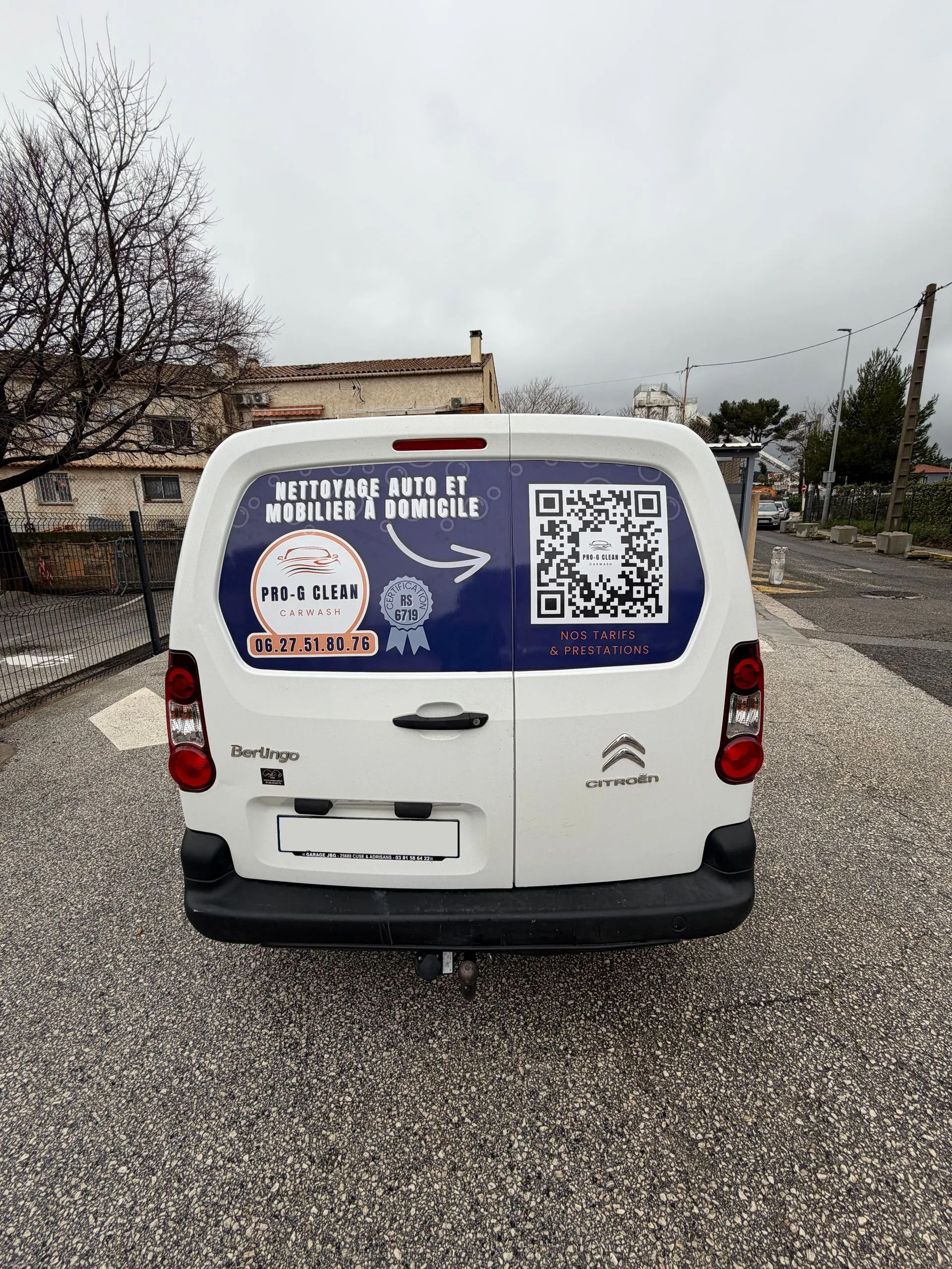 Fourgonnette Citroën blanche avec autocollants sur la lunette arrière, stationnée dans une rue.