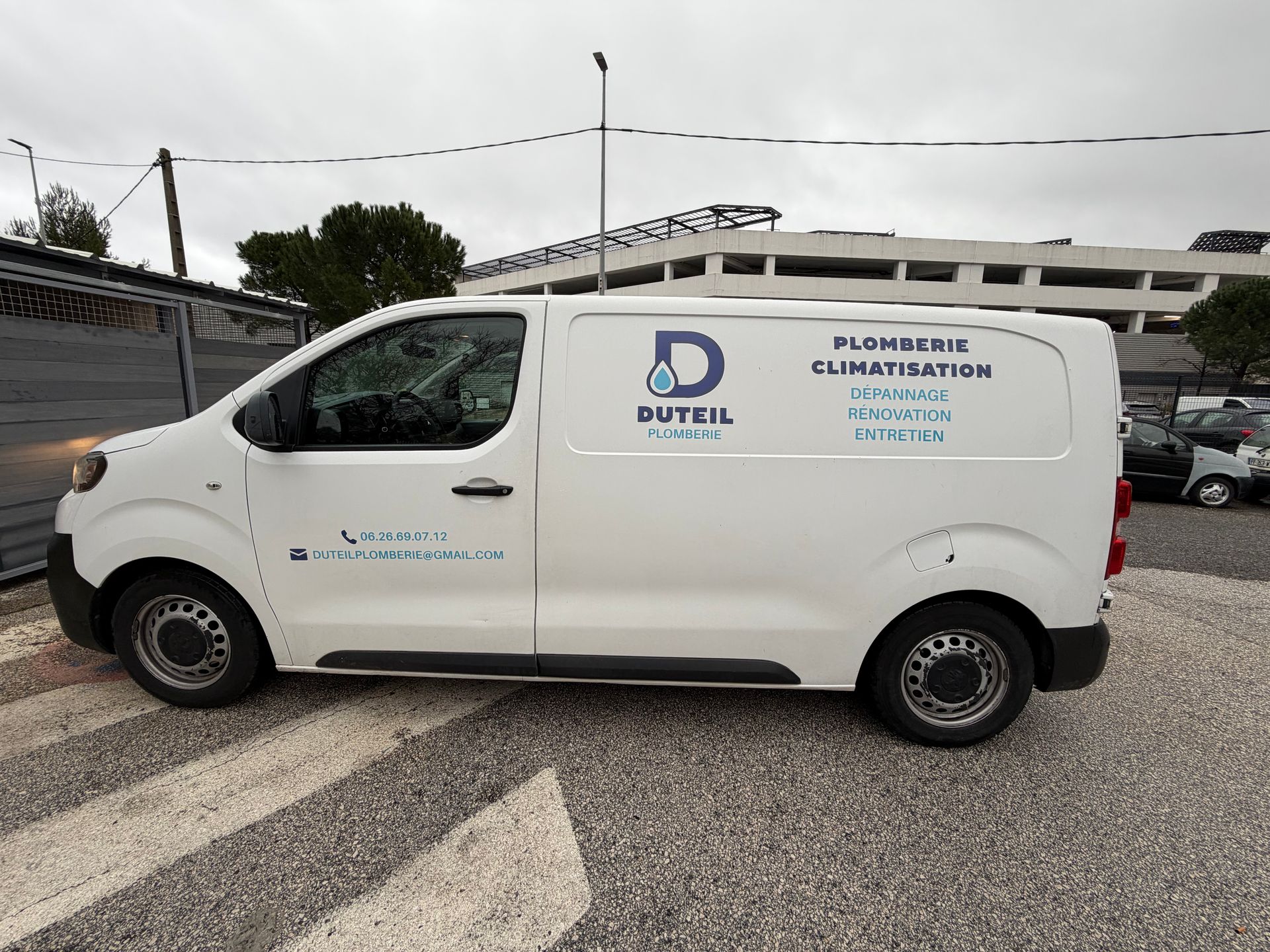 Une camionnette blanche portant le logo « Duteil » et des informations sur les services de plomberie est garée à l'extérieur.